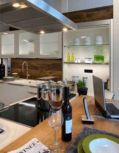 Eine Küche mit heller Verkleidung der Schränke und einer Holzplatte vorne rechts.
