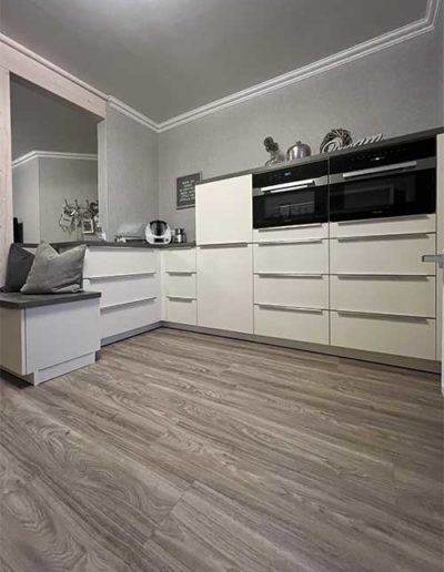 Eine weiße Küchenzeile mit eingebauten Backöfen auf grauem Parkettboden.
