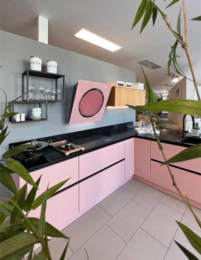 Eine moderne Küche mit rosafarbenen Schränken und schwarzen Platten. Die Dunstabzugshaube ist ebenfalls rosafarben.