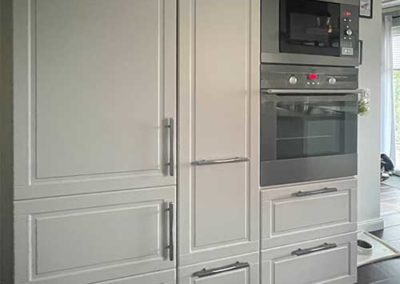 Ein großer Küchenschrank mit weißen Holztüren und eingebautem Backofen und Mikrowelle.