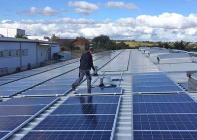 Ein Mann in Arbeitskleidung auf einem mit Photovoltaikplatten bedeckten Dach.