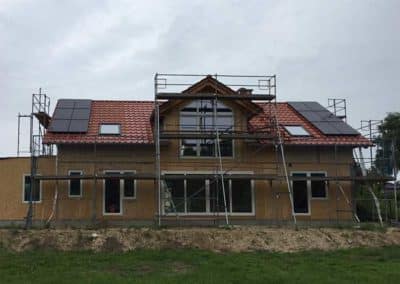 Ein von Gerüsten umgebenes Wohnhaus, dessen Dach mit Photovoltaik bestückt wird.