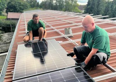 Zwei Männer in Arbeitskleidung, welche Photovoltaikplatten auf einem Dach anbringen.