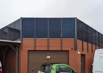Ein Geländer oberhalb einer geklinkerten Garage, welches aus großen schwarzen Stahlplatten und schwarzen Stahlpfosten besteht. Davor ein kleines Auto mit der Aufschrift "M+S Gruppe".
