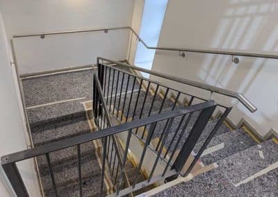 Ein Treppenhaus mit stählernem Handlauf und schwarzem, stählernem Geländer.