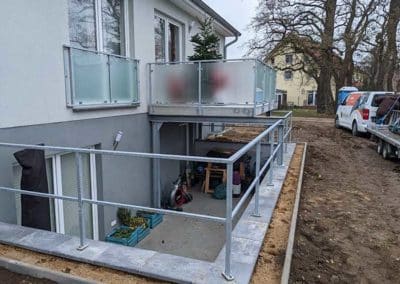 Stahlgeländer am Rand einer Absenkung eines Wohnhauses, über welchem ein Balkon mit Stahlgeländer angebracht ist.