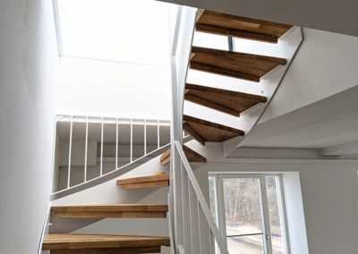 Eine Treppe mit weißem Stahlgeländer und hölzernen Stufen in einem Treppenhaus.